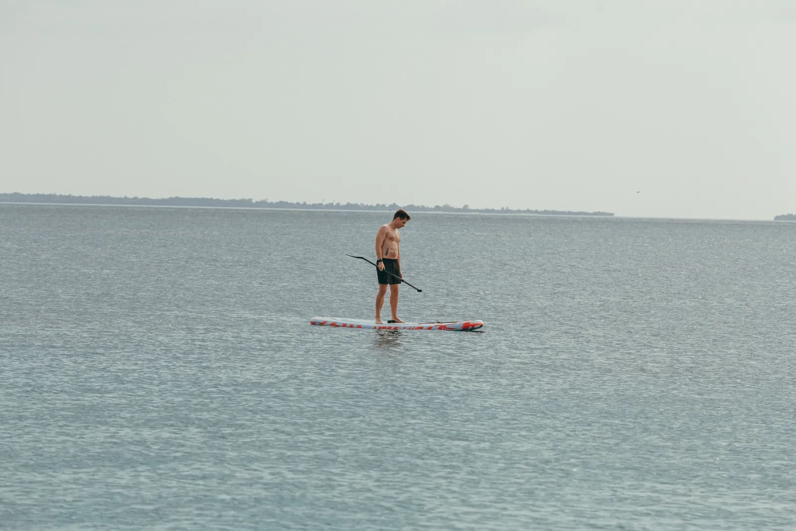 Young man standing on a paddle board in the middle of a calm ocean during a summer vacation