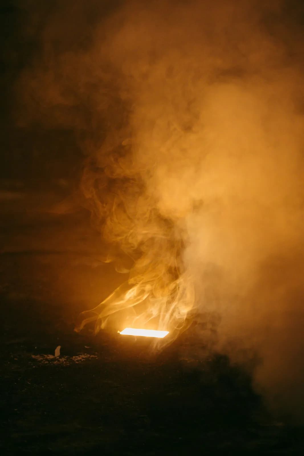 Bright glowing light source emitting thick orange smoke in a dark industrial setting
