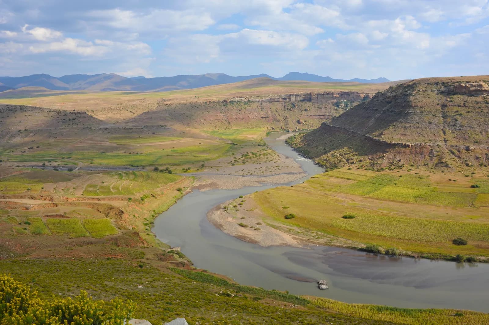 Scenic winding river through arid canyon landscape with green meadows and rocky cliffs