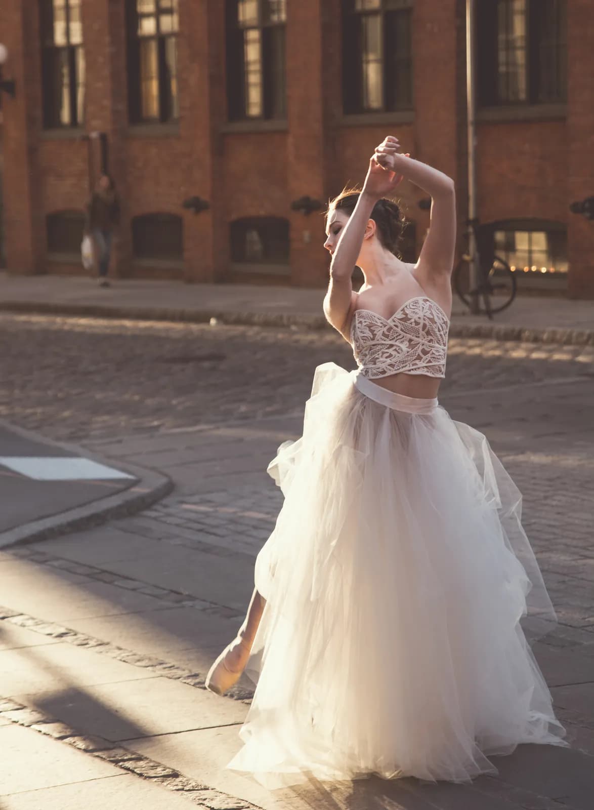 Graceful ballerina dancing in white tulle dress on cobblestone street during golden hour sunlight