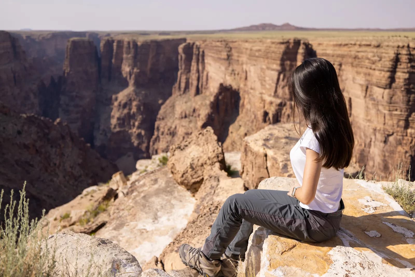 Young woman sitting on a cliff edge looking at a deep canyon landscape during a summer hiking trip