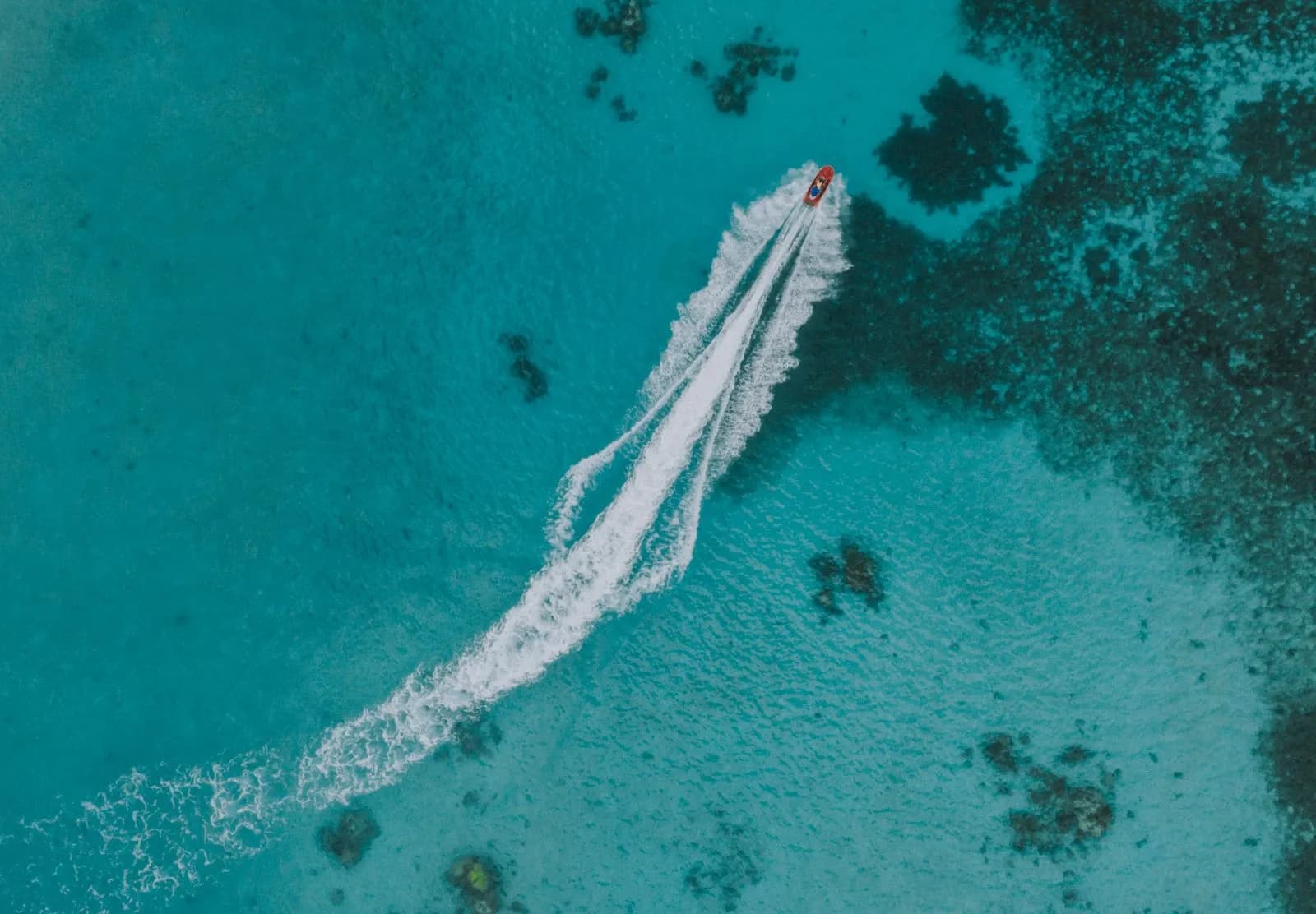 Aerial view of a small motorboat cruising fast over turquoise tropical ocean water with coral reefs