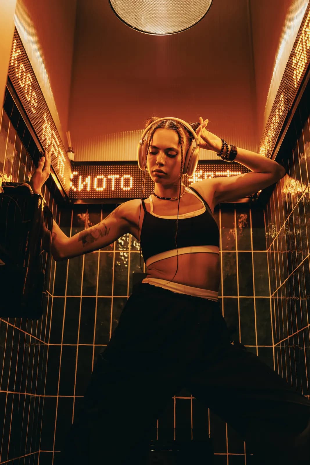 Young woman listening to music with headphones in a dark tiled room with warm neon lighting