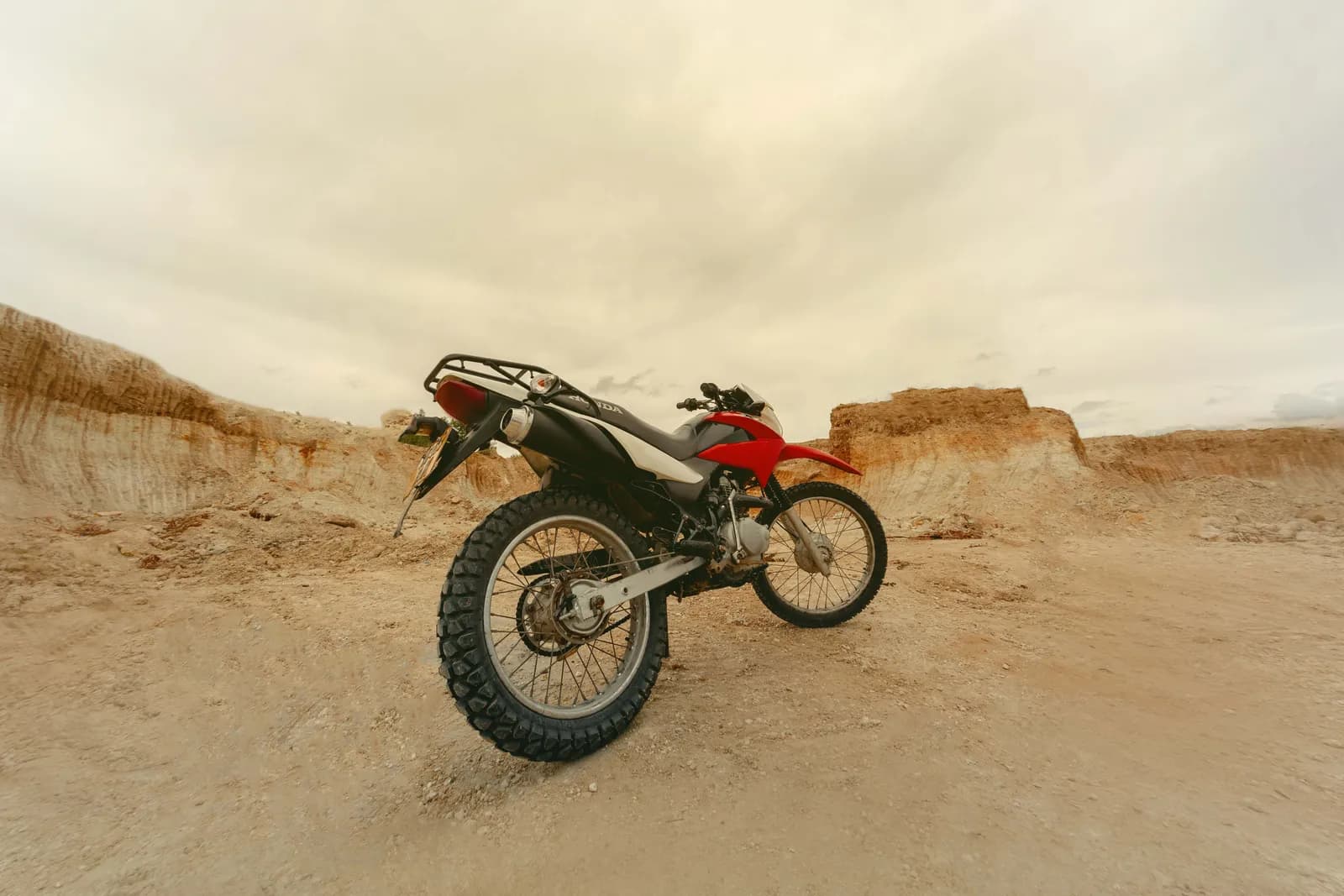 Red dirt bike parked on sandy desert terrain under cloudy sky for adventure travel and sport concept
