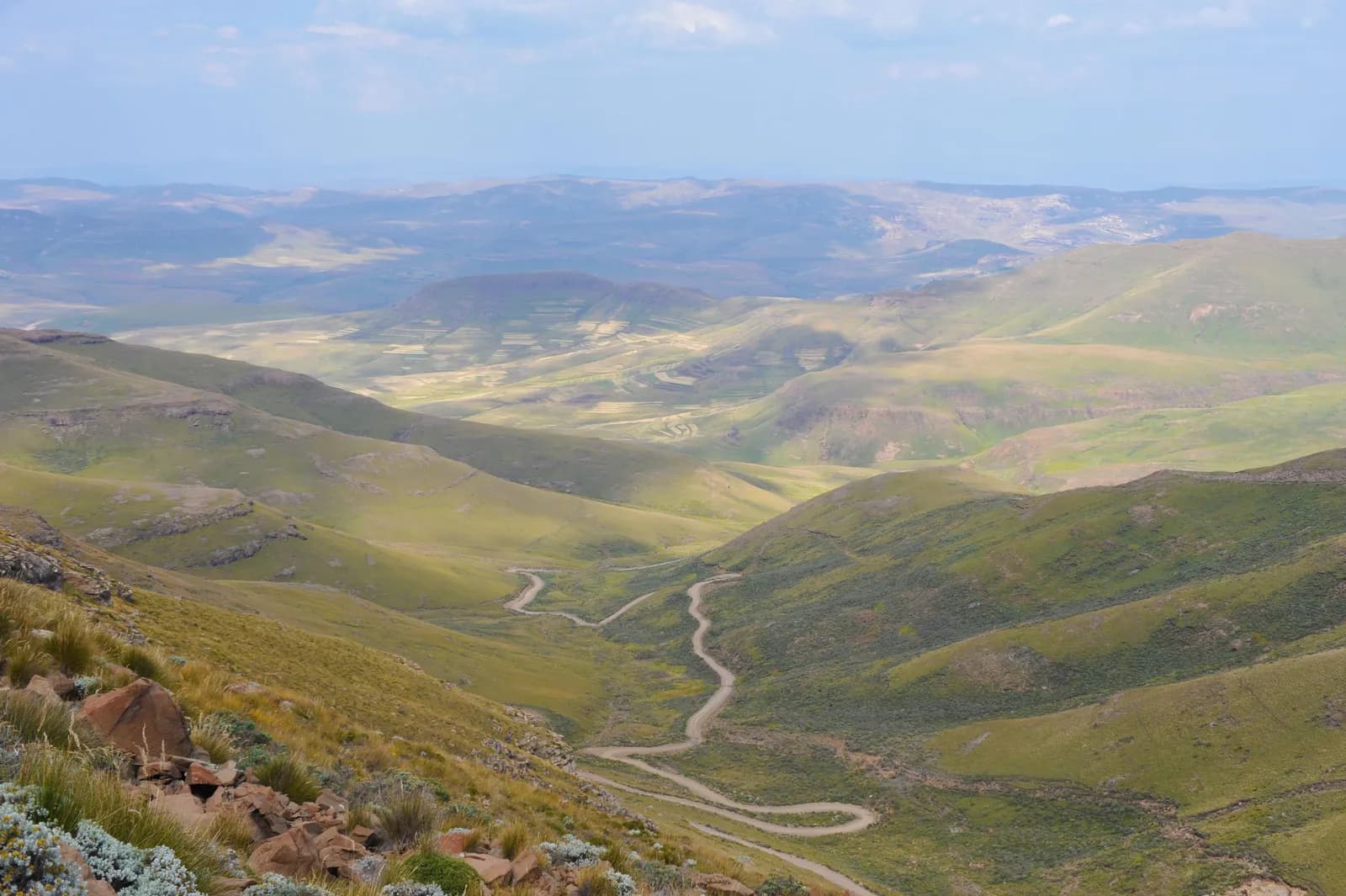 Winding dirt road through green mountain valley landscape under a clear blue sky in summer