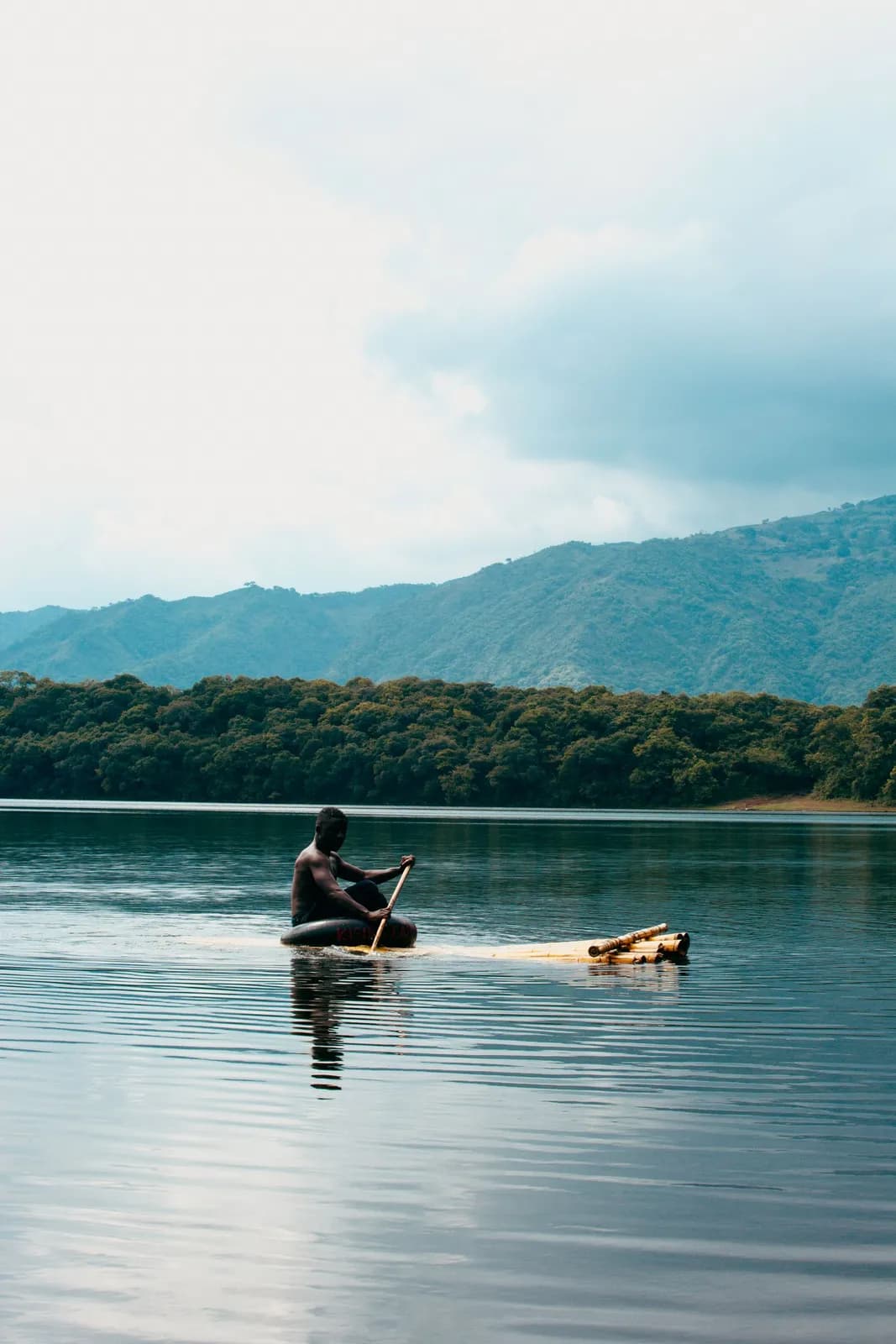 African fisherman paddling a wooden raft on a calm lake with mountain background for travel concepts