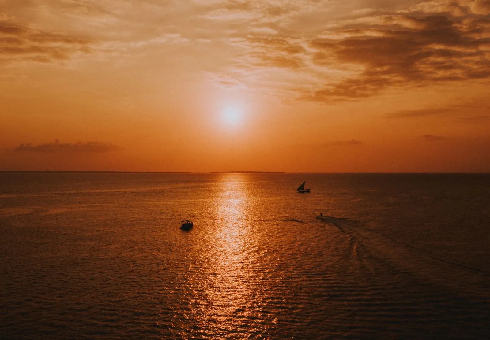 Golden sunset over the ocean with small boats sailing on calm water during a peaceful evening