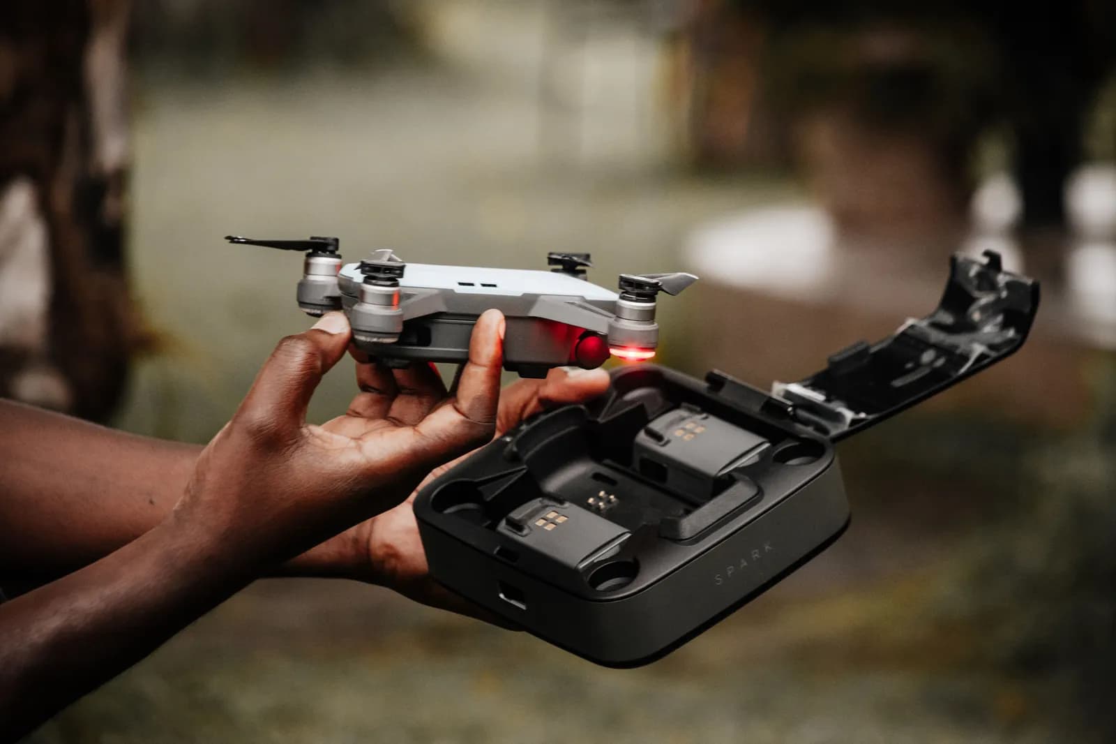 Person holding a small drone and charging case outdoors for aerial photography preparation