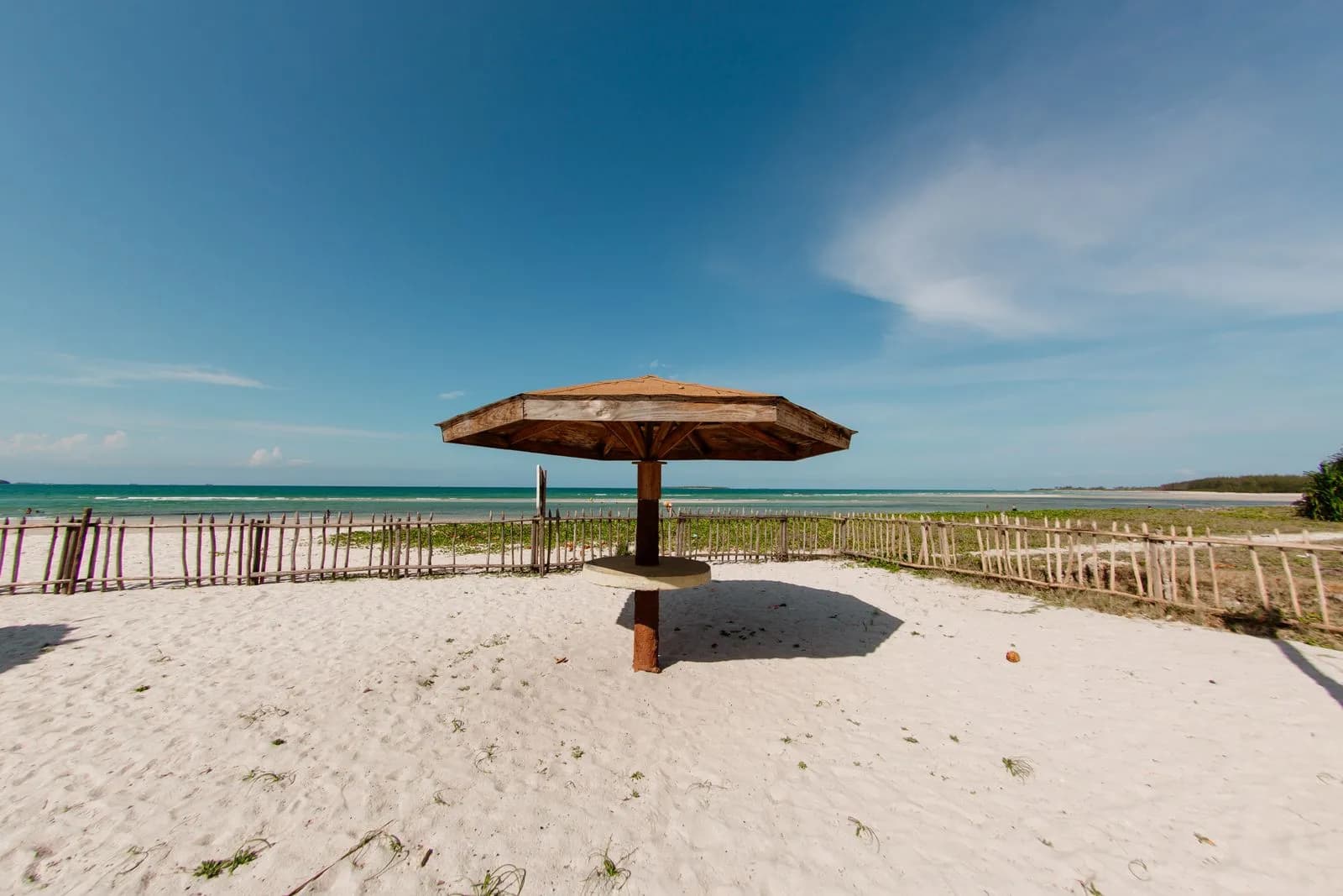 Wooden beach umbrella on white sand tropical shore with blue ocean and clear sky background