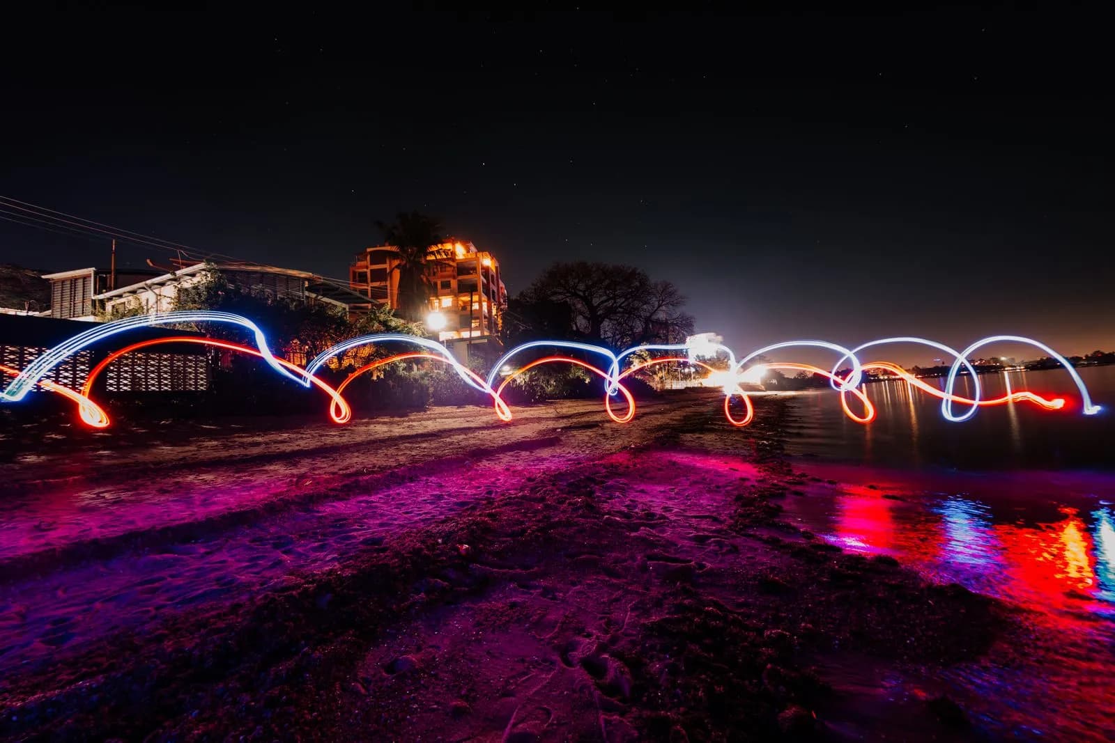 Long exposure light painting trails on a dark beach at night with glowing red and blue neon lights
