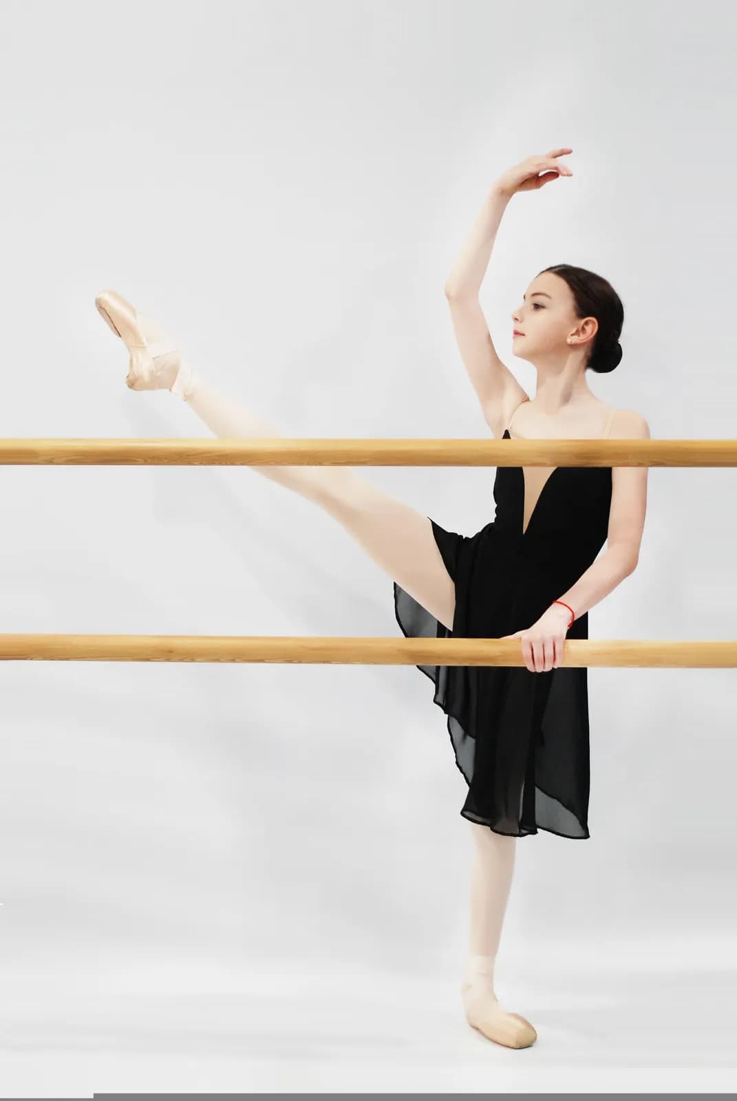 a young female dancer in a black leotard practicing ballet movements at a wooden barre