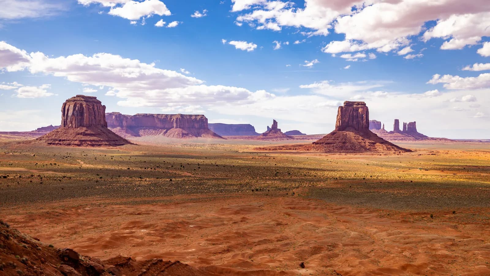 Scenic view of monument valley buttes under a bright blue sky with clouds in the arizona desert