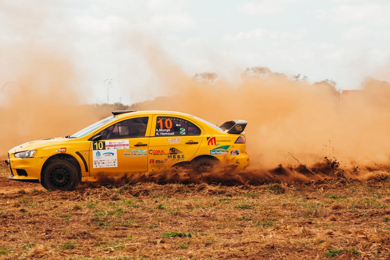 Yellow rally car drifting on dirt track during professional off road racing competition event