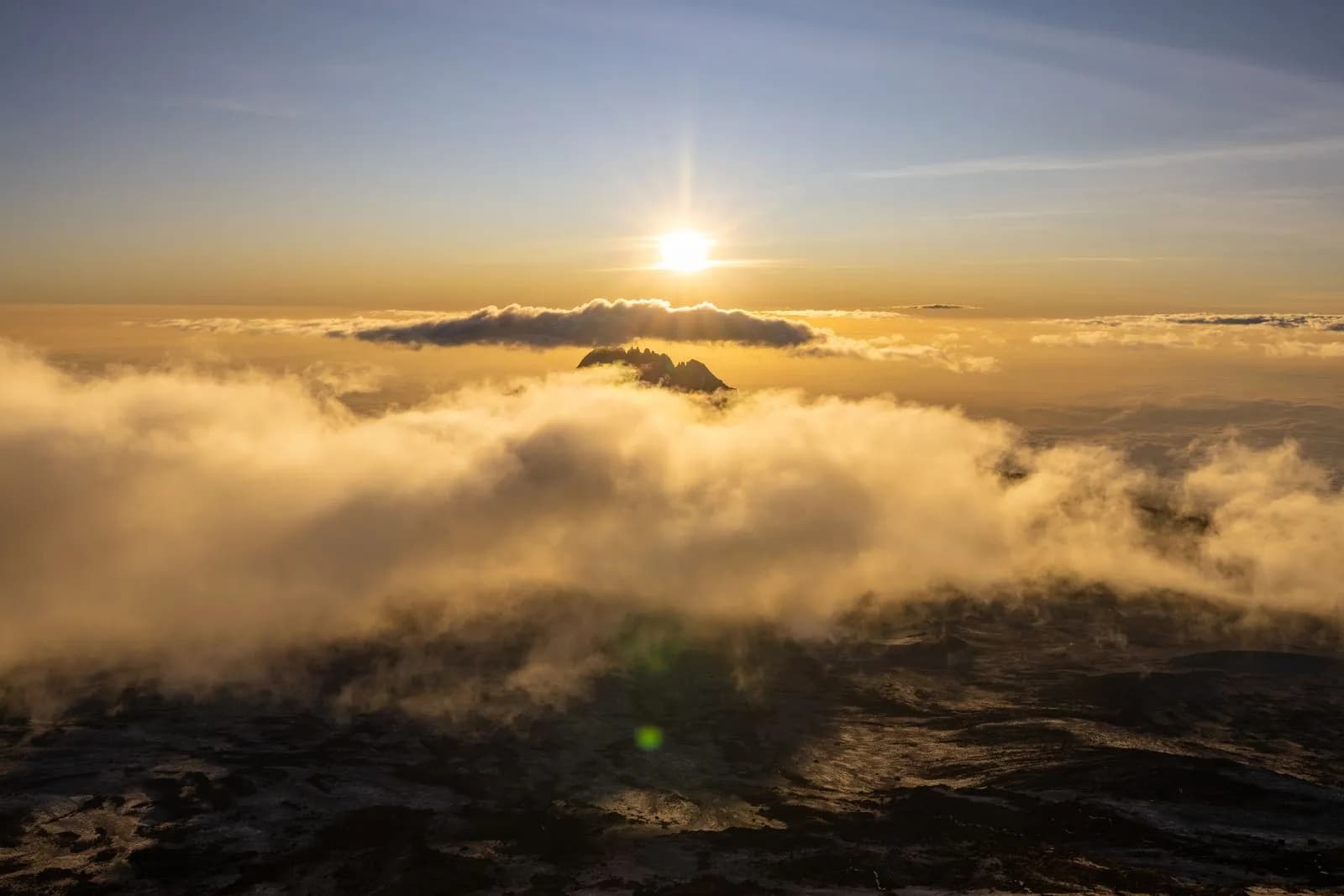 Aerial view of mountain peak rising above golden clouds at sunrise