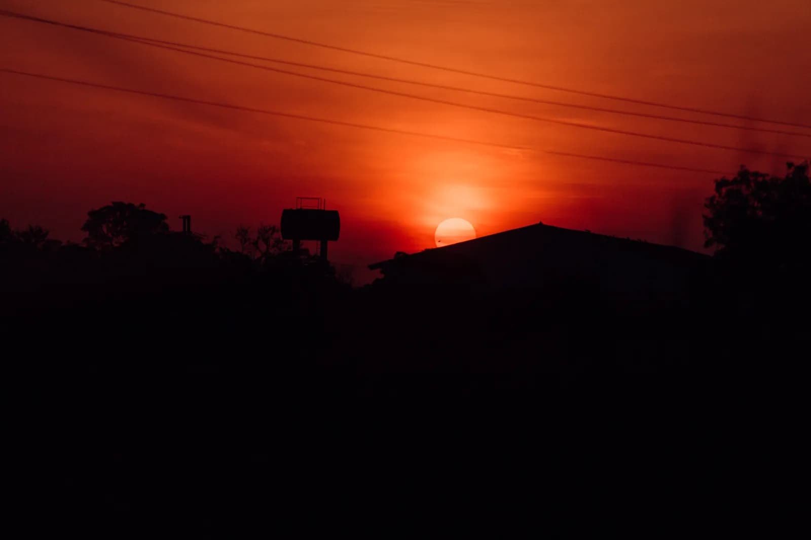 Vibrant orange sunset sky with silhouette of house and water tank in rural landscape setting