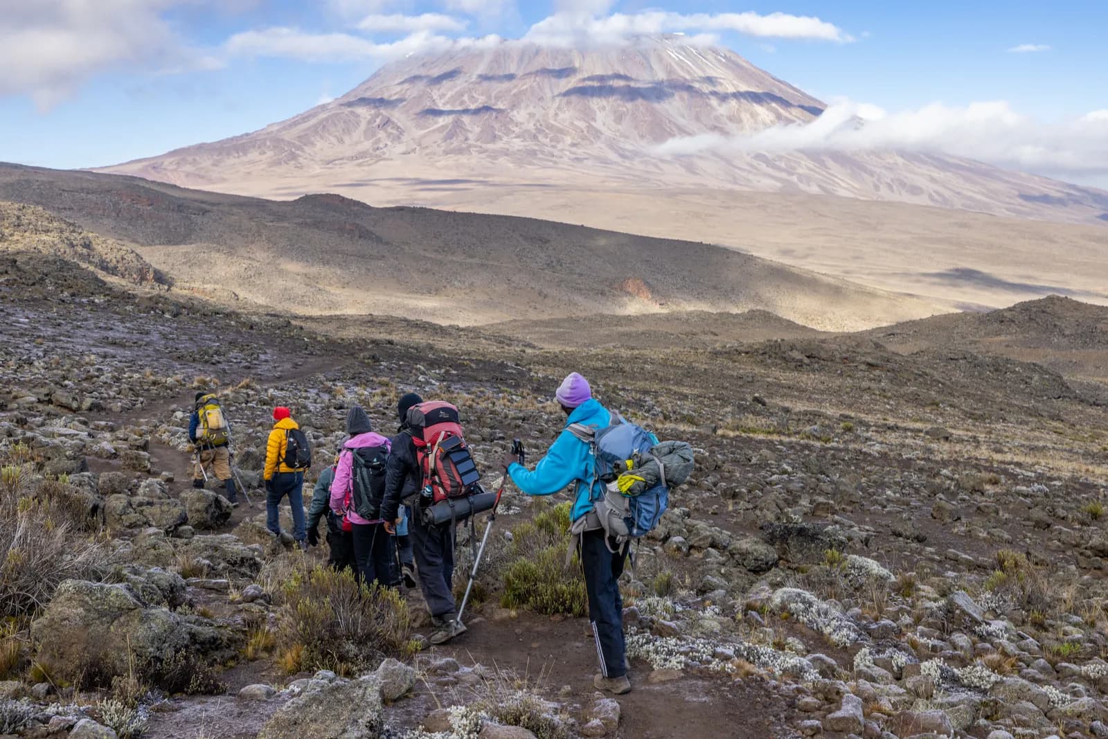 Group of hikers trekking on a mountain trail towards a volcanic peak in tanzania