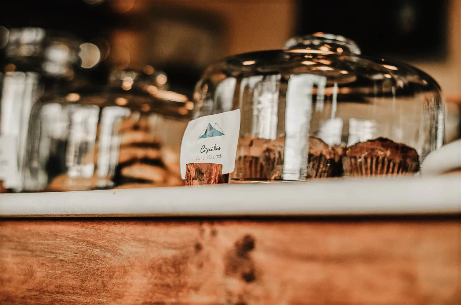 Freshly baked chocolate muffins displayed on wooden counter with glass dessert containers