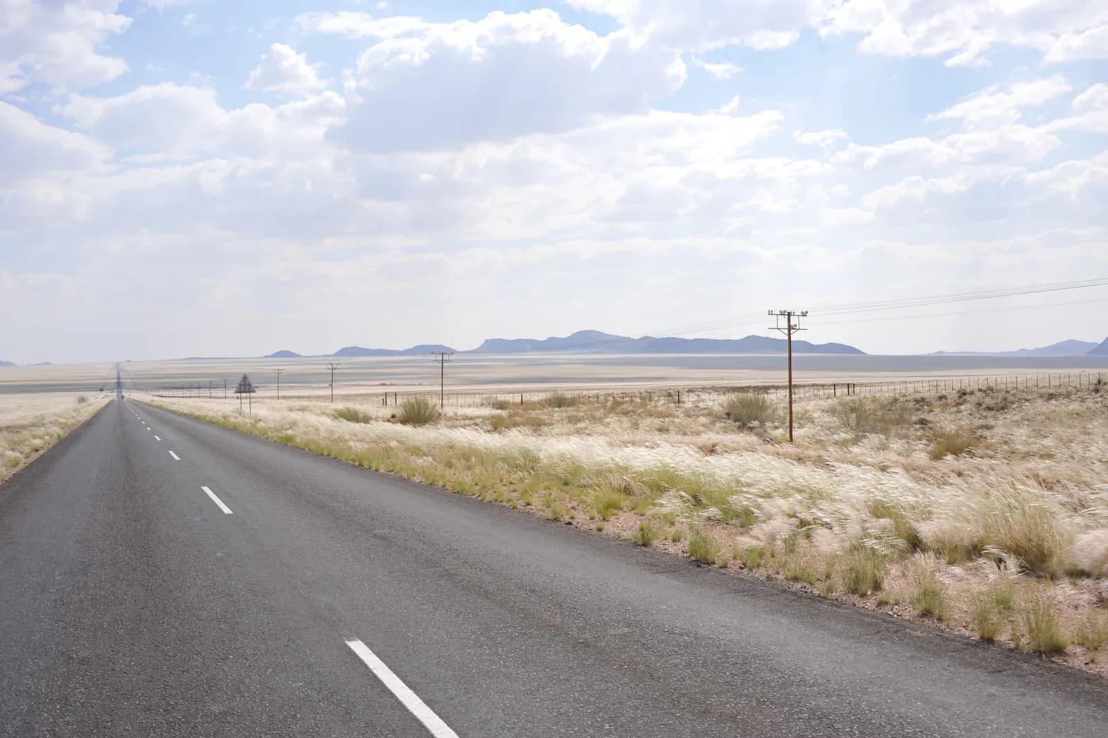 Asphalt road stretching through a vast arid desert landscape under a bright cloudy sky