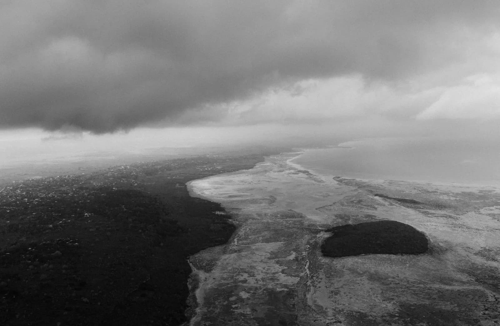 Aerial view of a tropical coastline with dark storm clouds gathering over the ocean and forest