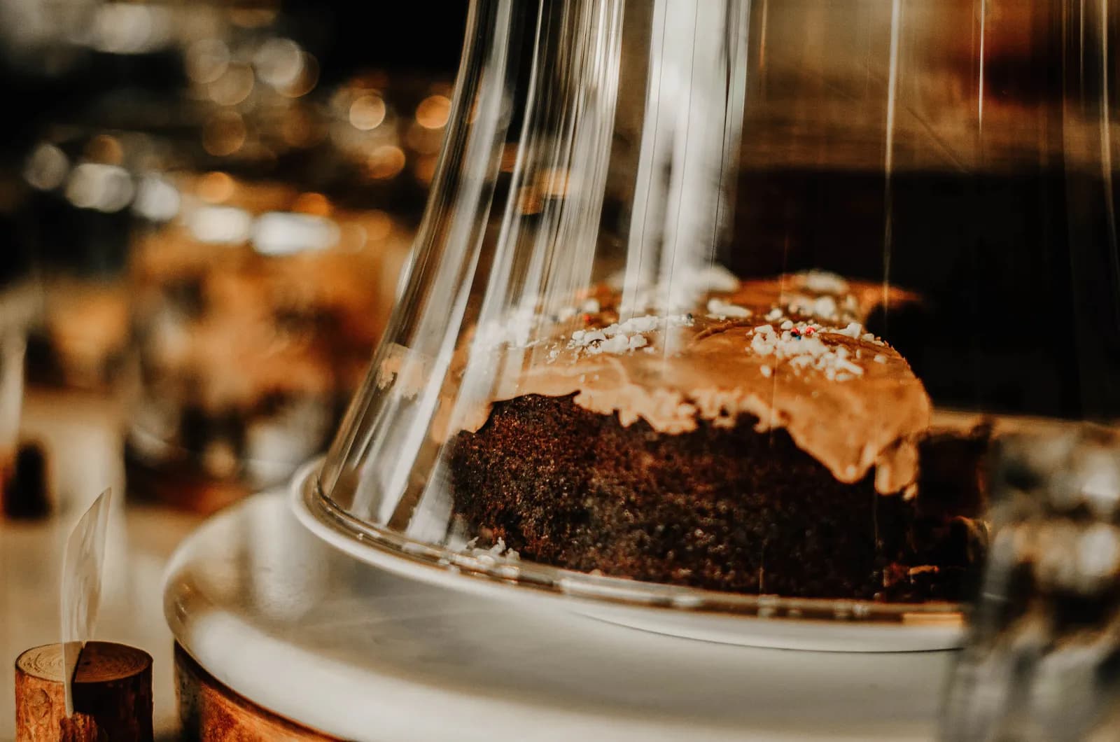 Chocolate cake slice under glass dome in cozy restaurant dessert display
