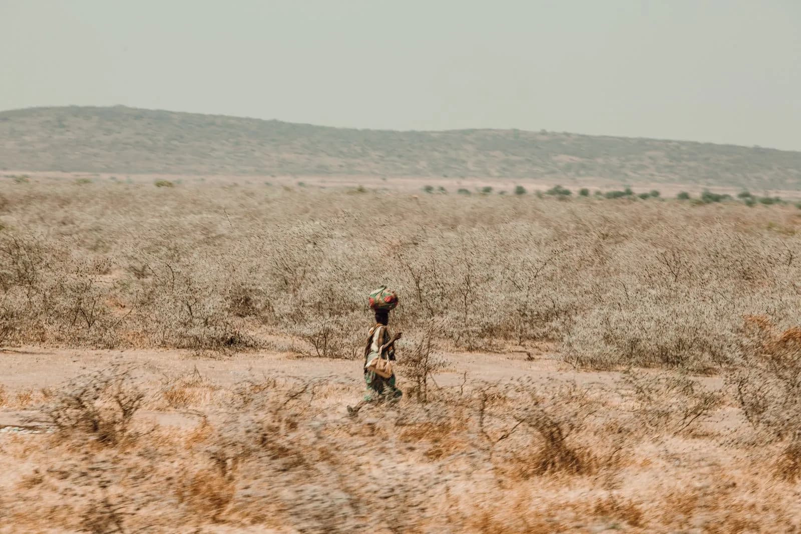 African woman carrying goods on her head walking through a dry arid landscape in rural ethiopia