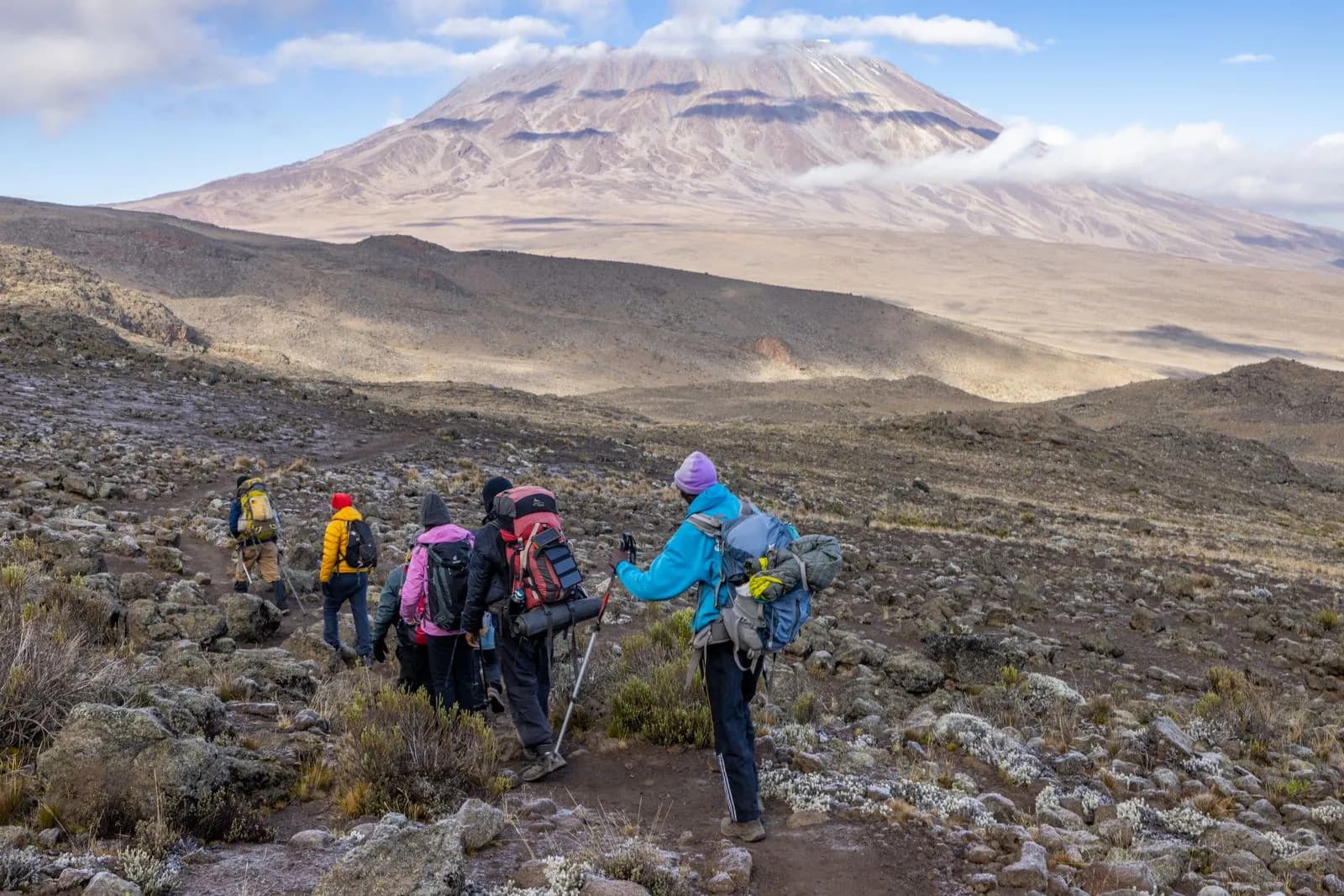 Group of hikers trekking on a rocky mountain trail towards a large volcanic peak in tanzania
