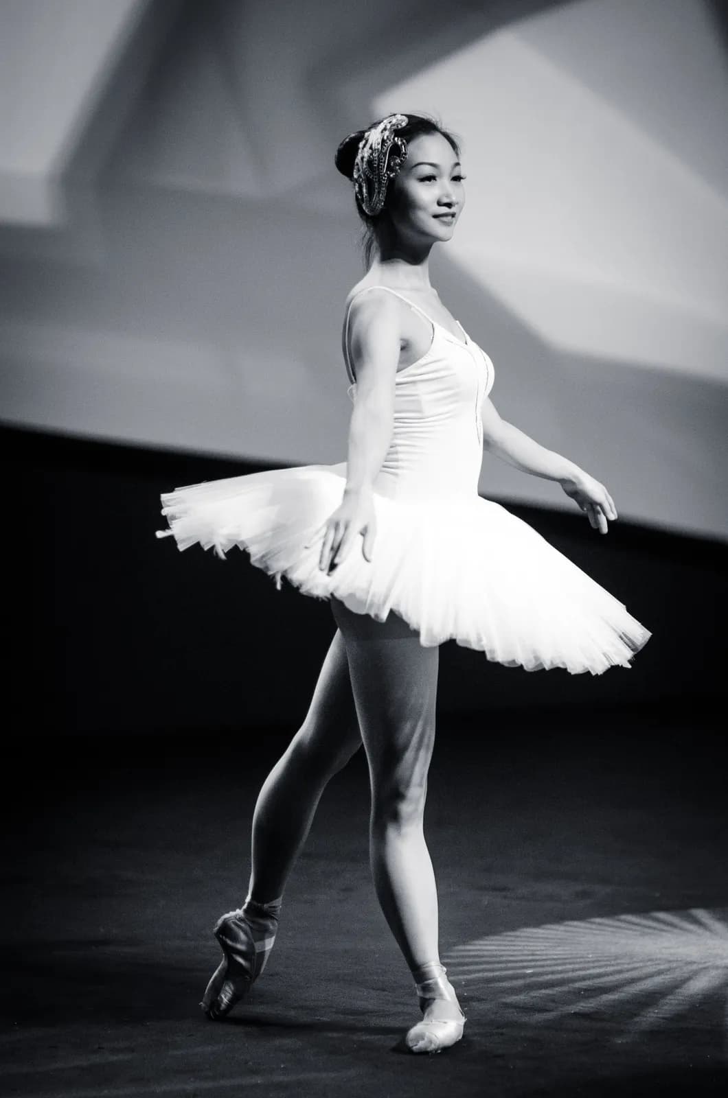 Young asian ballerina performing classical ballet dance on stage in white tutu and pointe shoes