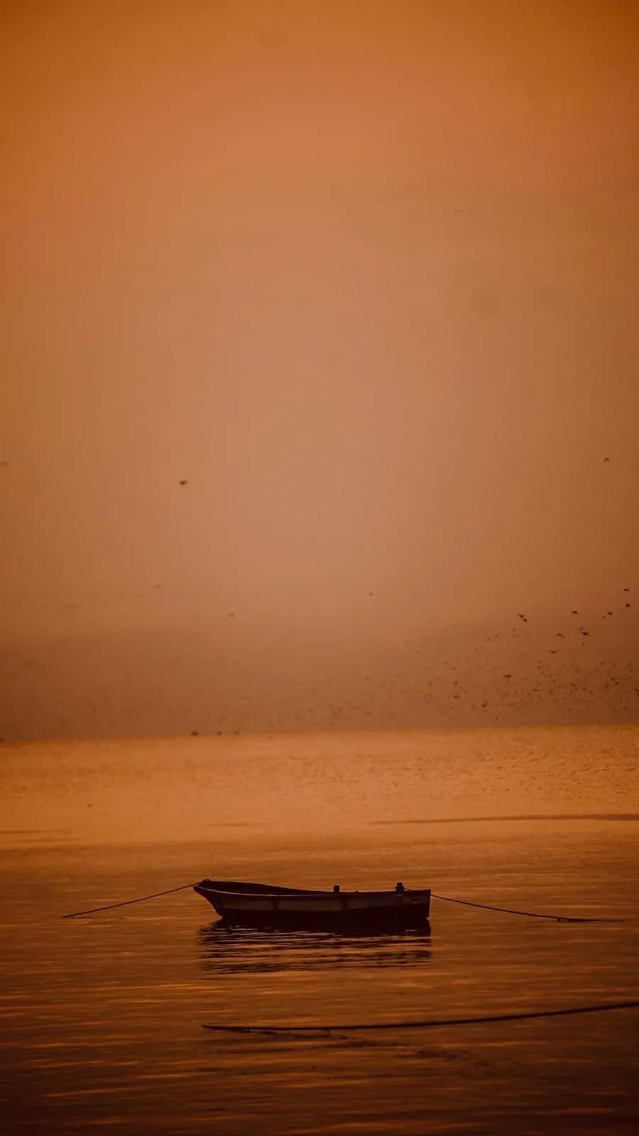Small fishing boat floating on calm water during a peaceful golden sunset at the ocean horizon