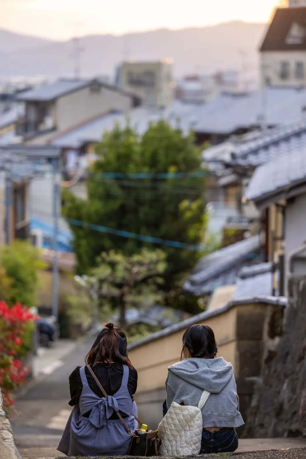 Two young women sitting on stone steps overlooking a traditional japanese town at sunset