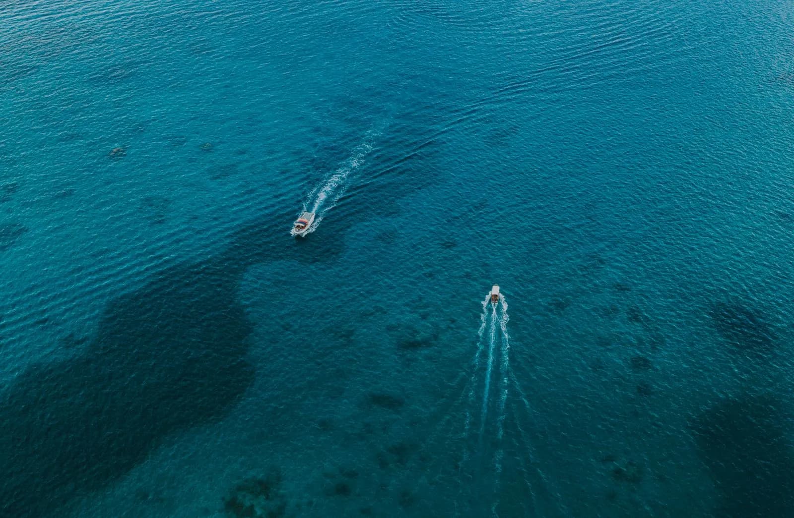 Aerial view of two small motorboats cruising across clear blue tropical ocean water