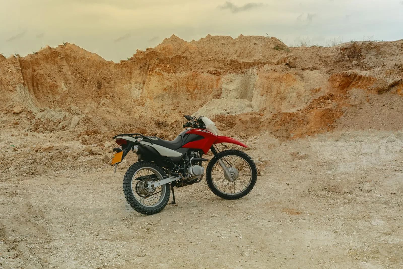 Red dual sport motorcycle parked on a dirt track in a rocky quarry landscape for adventure travel