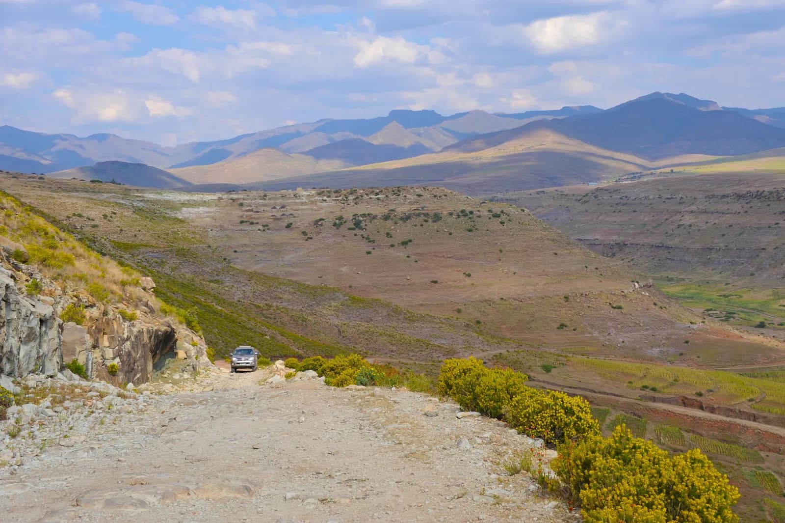 Silver suv driving on a remote dirt road through a vast mountain landscape during the daytime