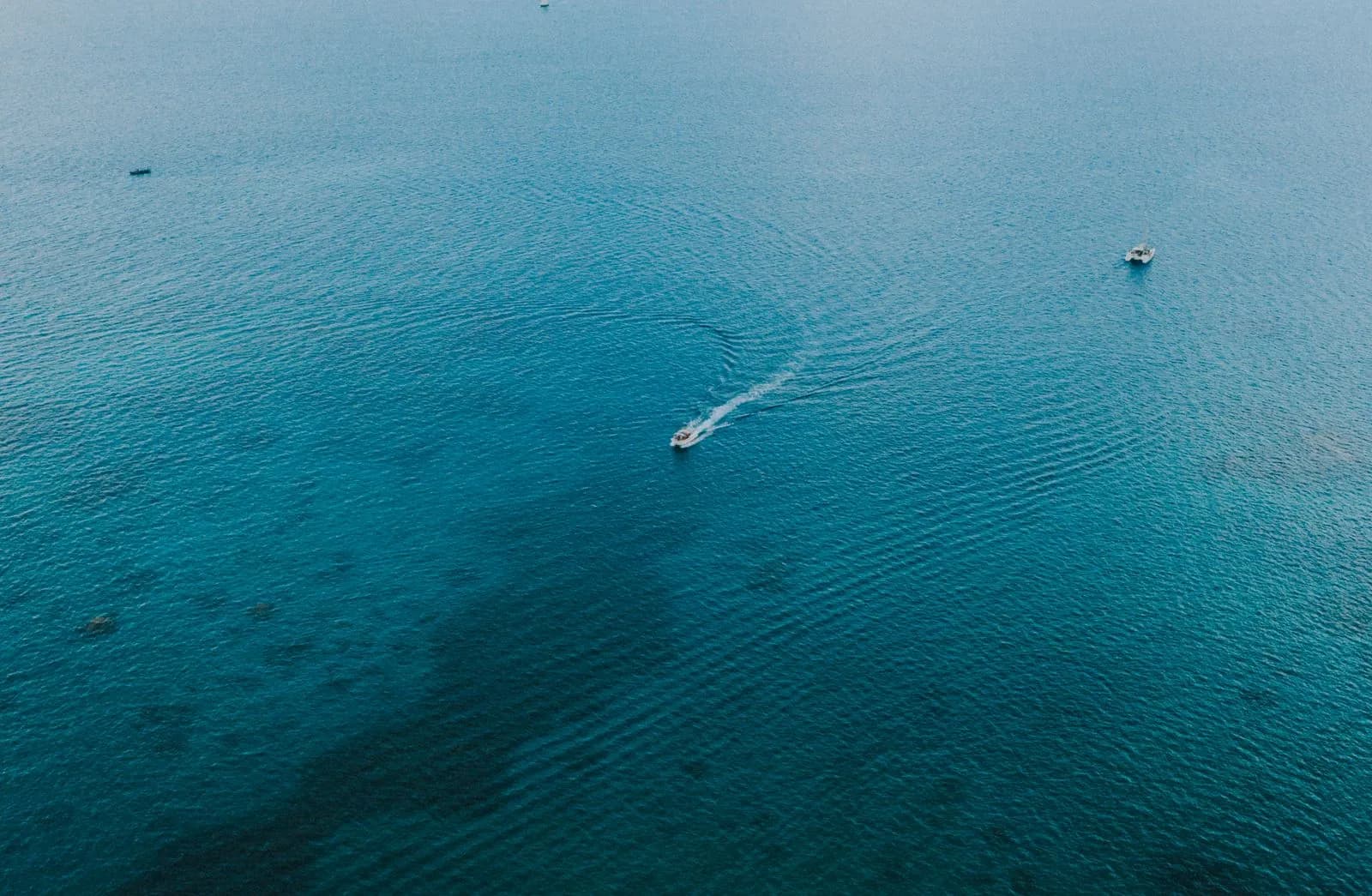 Aerial view of a small motorboat cruising across the deep blue tropical ocean water surface