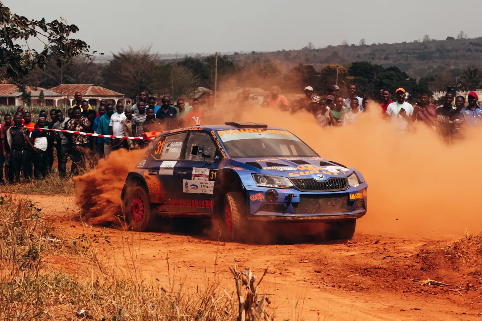 Blue rally car drifting on a dirt track during a professional racing competition with spectators