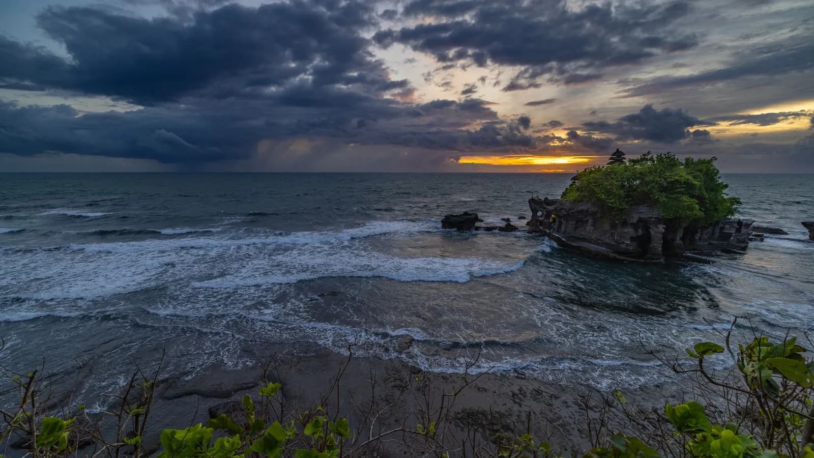 Dramatic sunset over tanah lot temple on bali island with ocean waves and cloudy sky at dusk