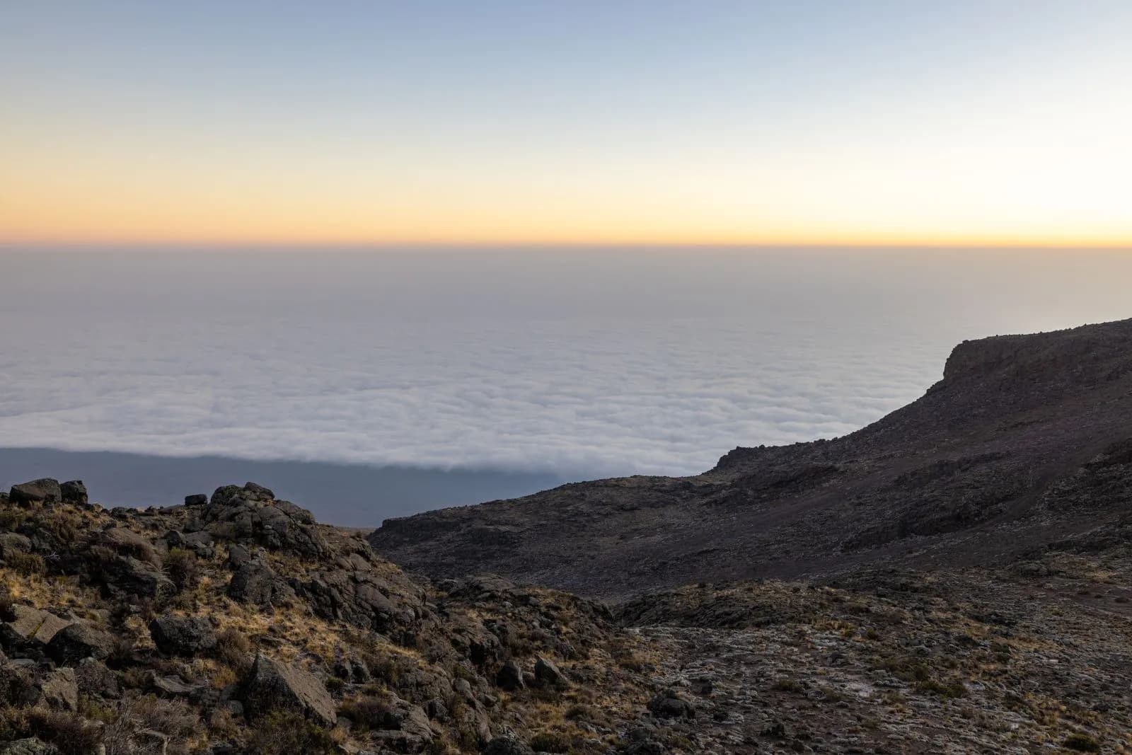 Panoramic view of mountain peak above thick clouds at sunrise with golden horizon light