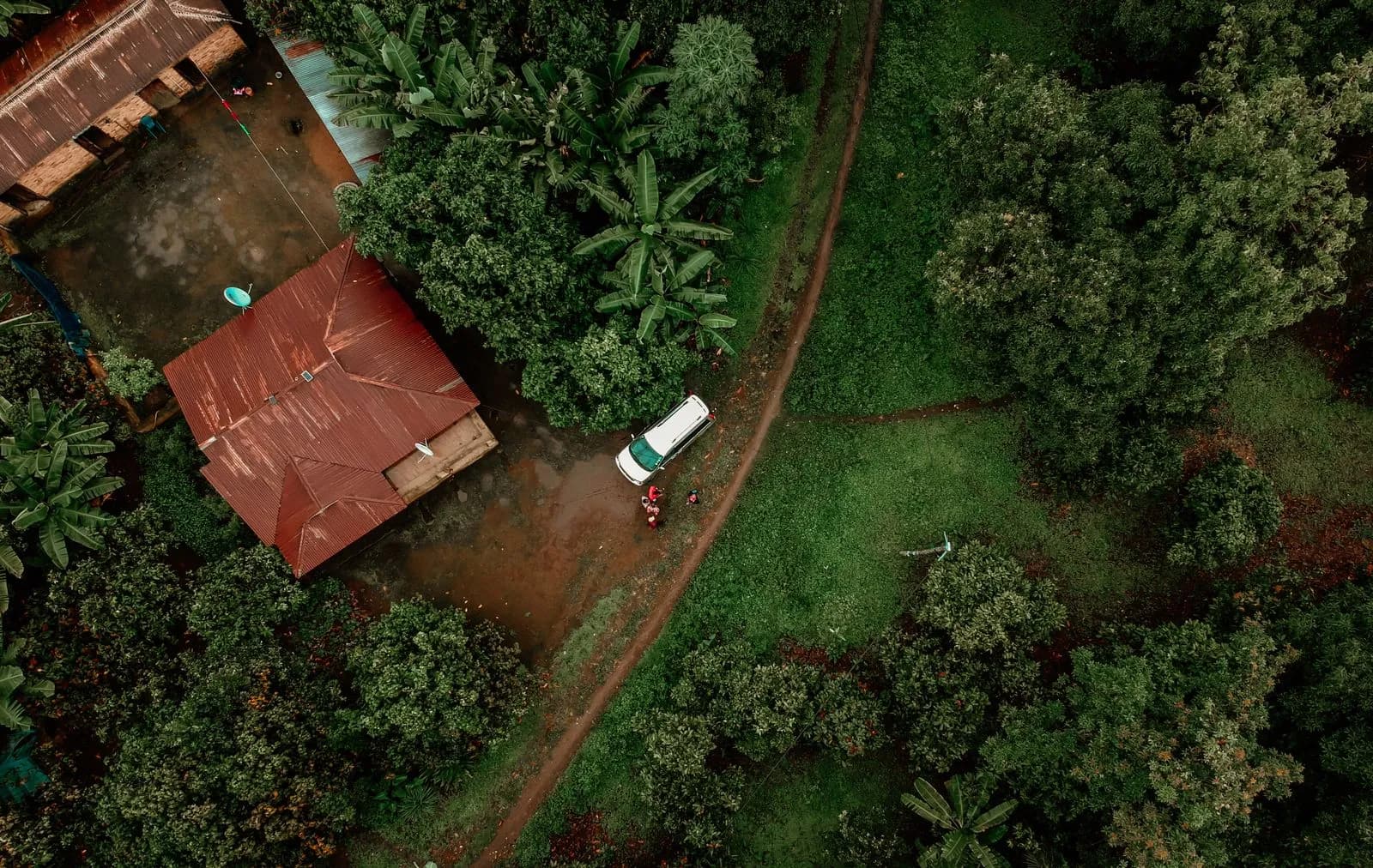 Aerial view of a white van parked near a rural house surrounded by lush green tropical vegetation