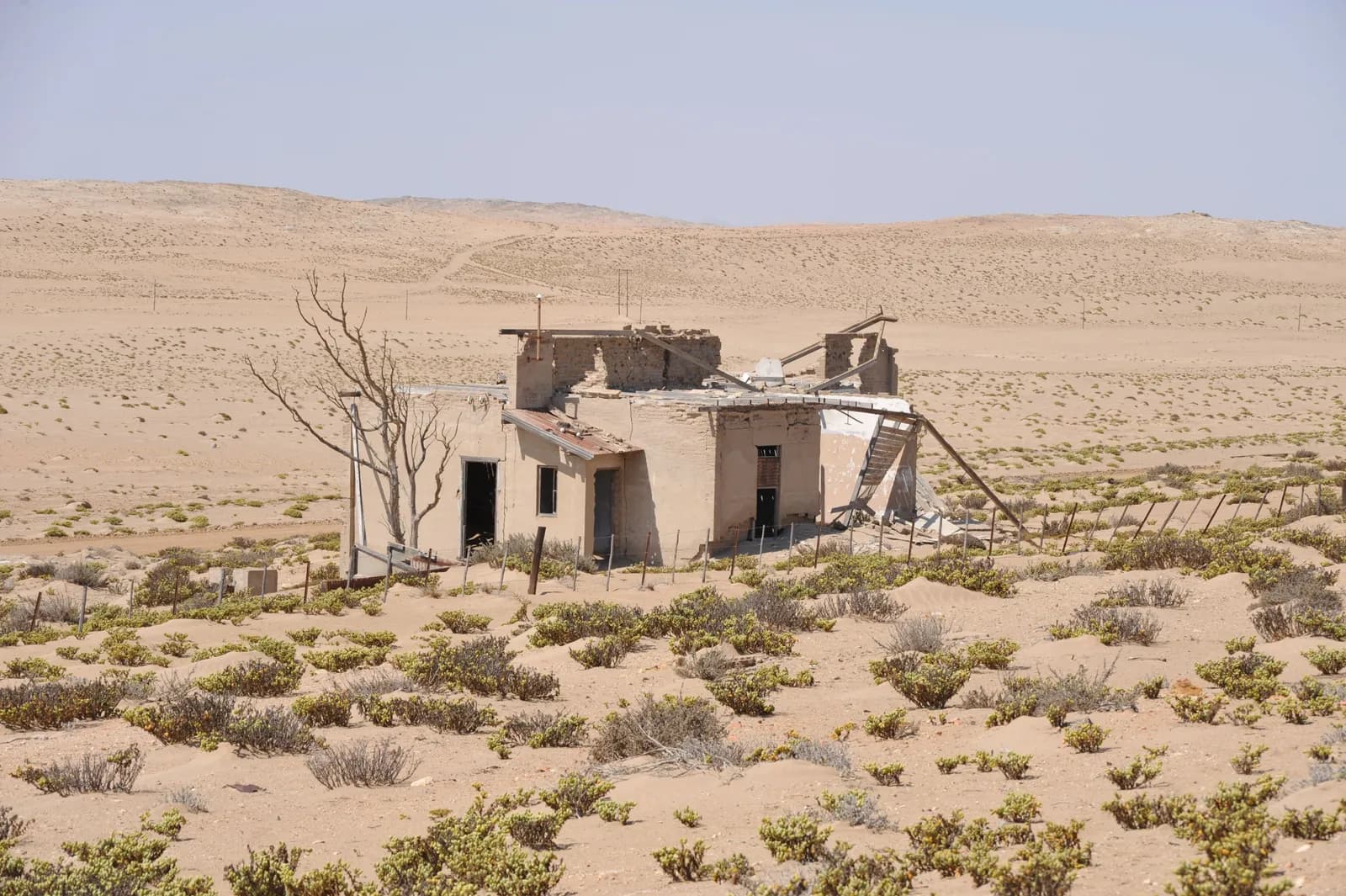Abandoned house in the middle of a dry desert landscape with sparse vegetation and clear blue sky
