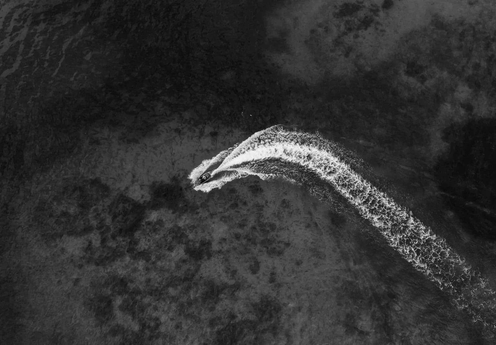 Aerial view of a small motorboat creating a white wake in dark tropical ocean waters