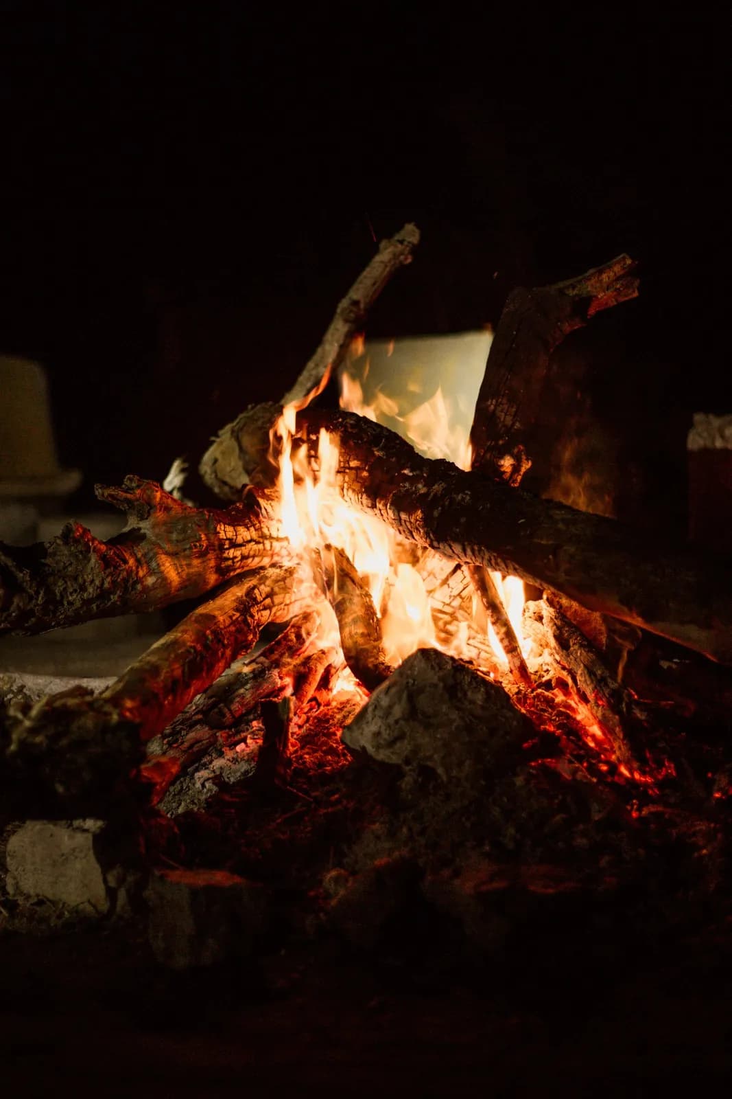 Bright burning campfire with glowing orange flames and logs at night in a dark outdoor setting