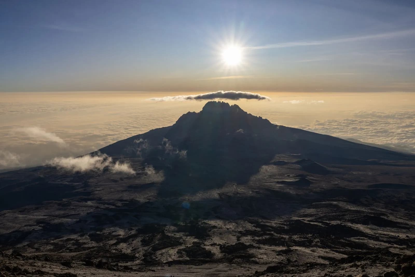 Majestic volcanic mountain peak rising above clouds with golden sun rays