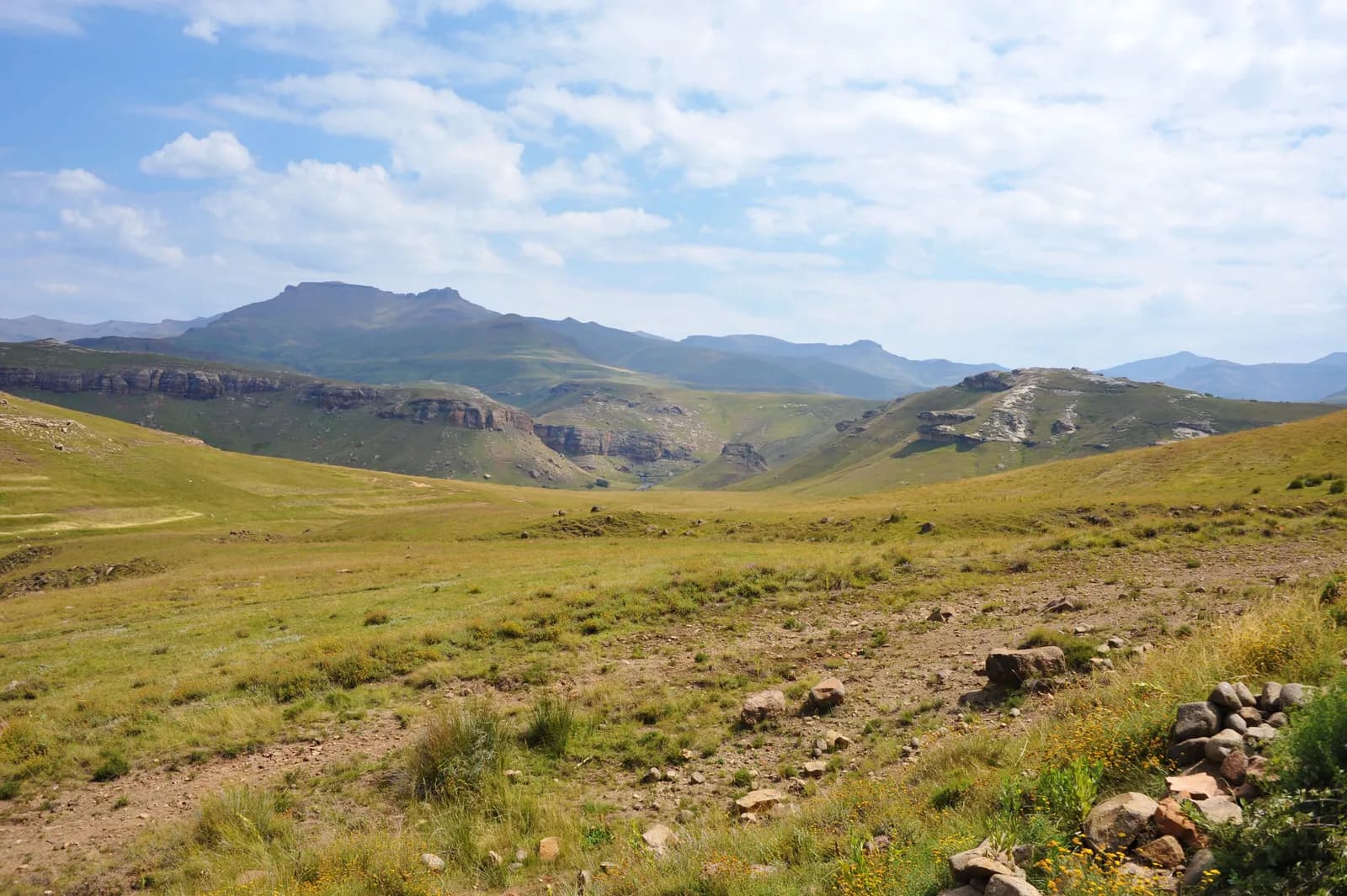 Scenic landscape view of golden grassy hills and rocky mountains under a blue sky with white clouds