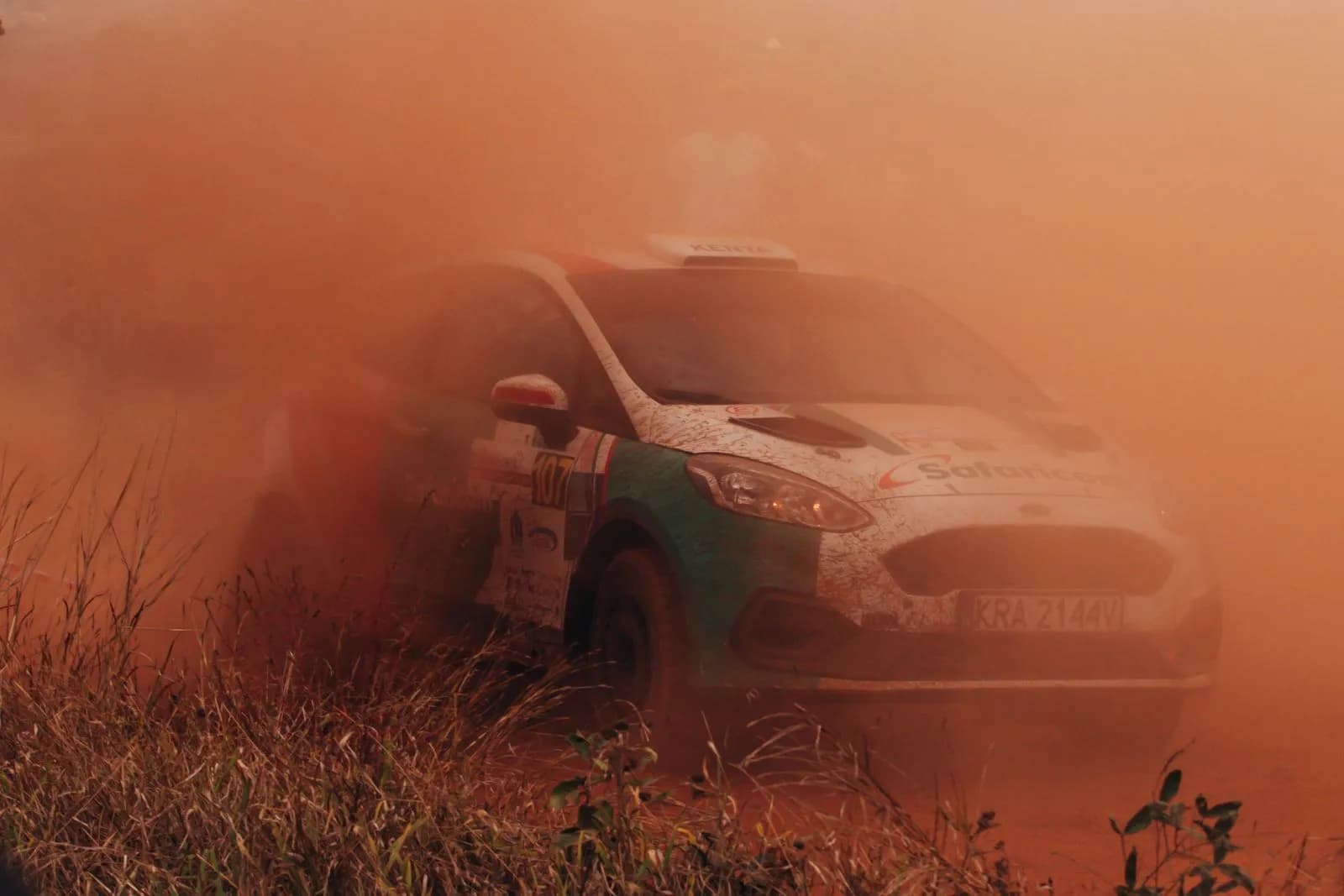 Rally car driving fast on dirt track creating thick dust cloud during professional racing competition