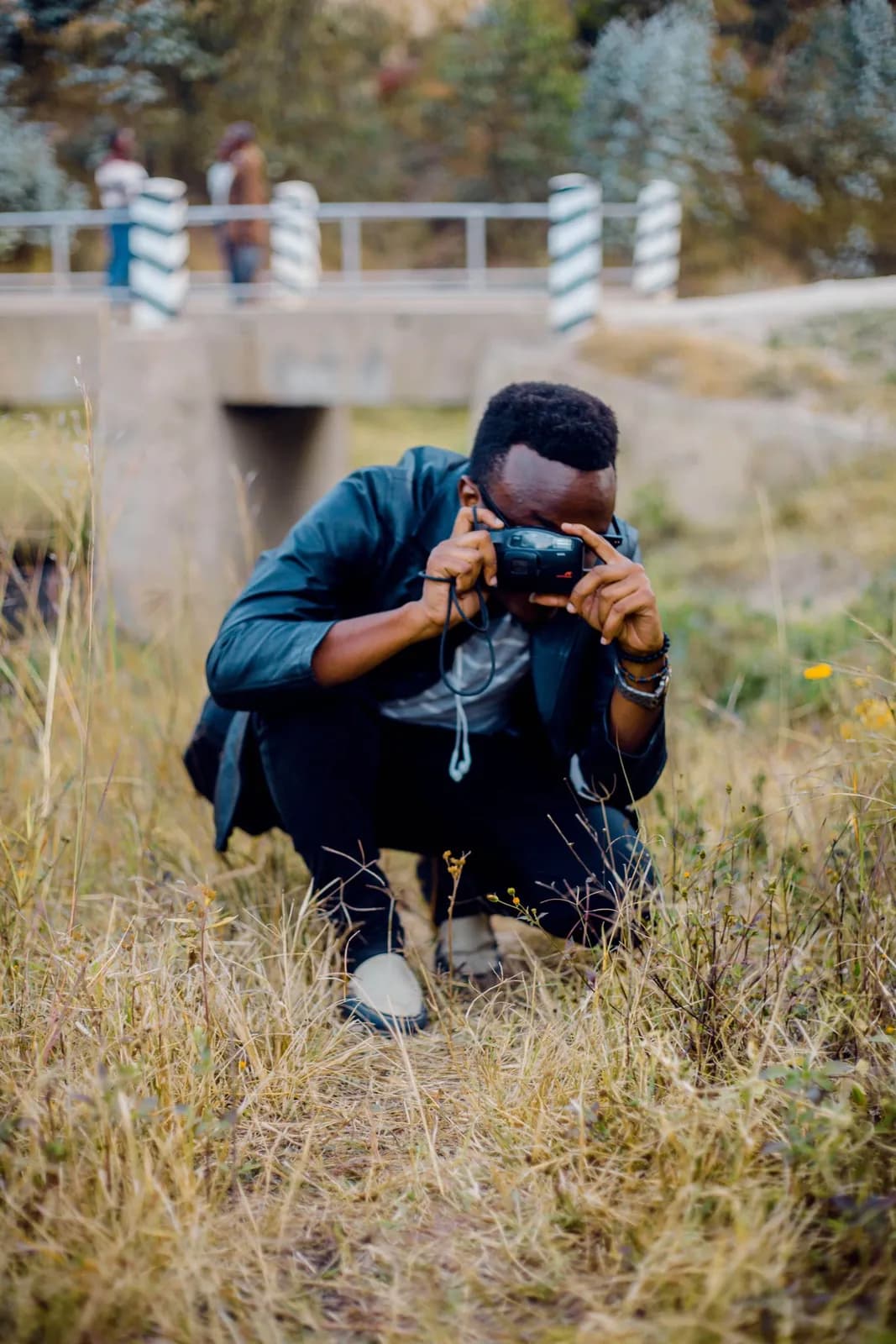 Young african man crouching in a field taking pictures with a vintage film camera outdoors