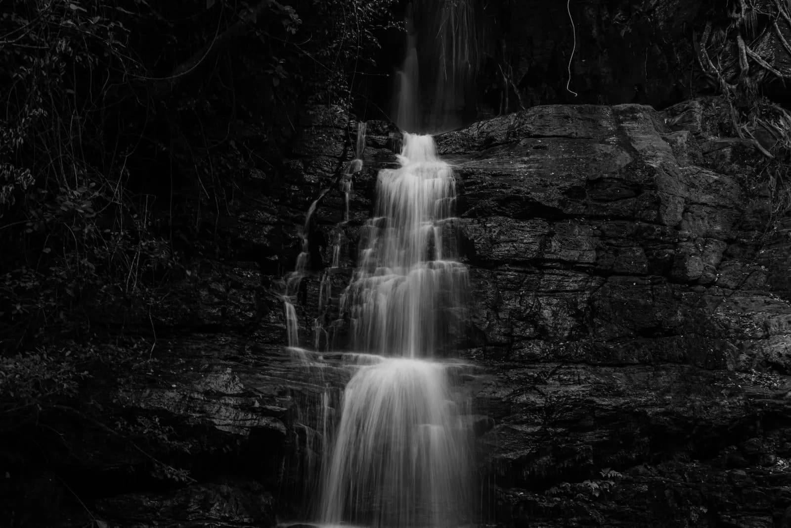Black and white long exposure of a cascading waterfall flowing over dark textured rocky cliff face