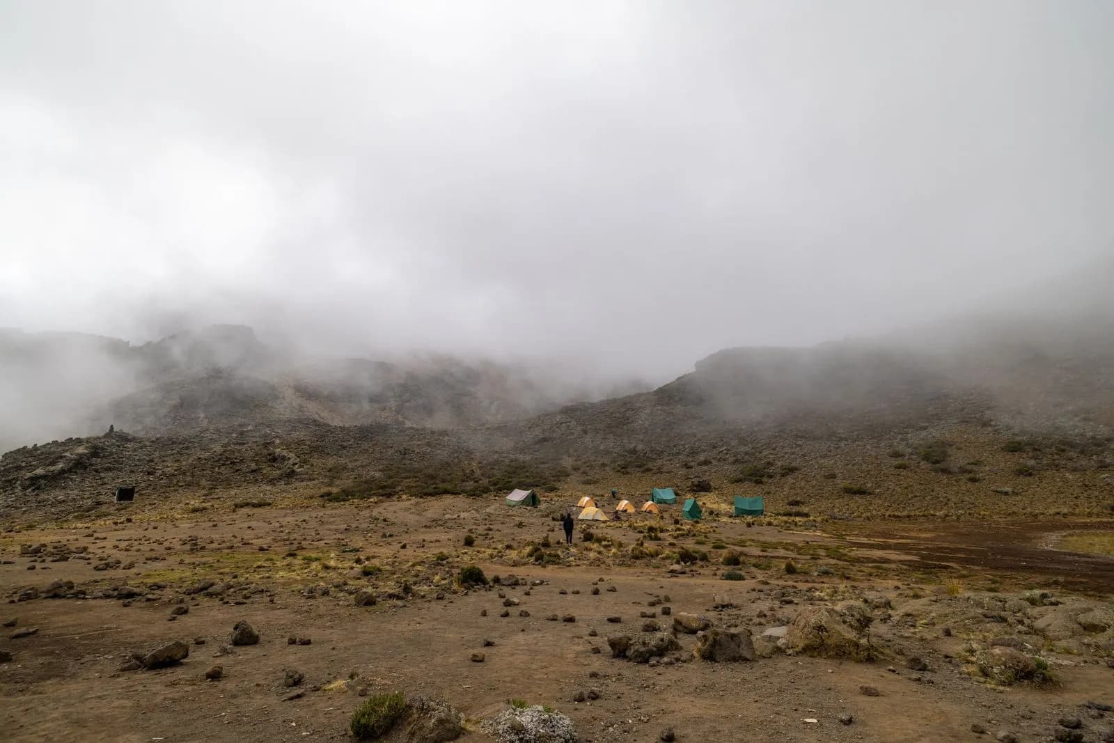 Small camping tents set up on a rocky mountain landscape under heavy fog and cloudy sky