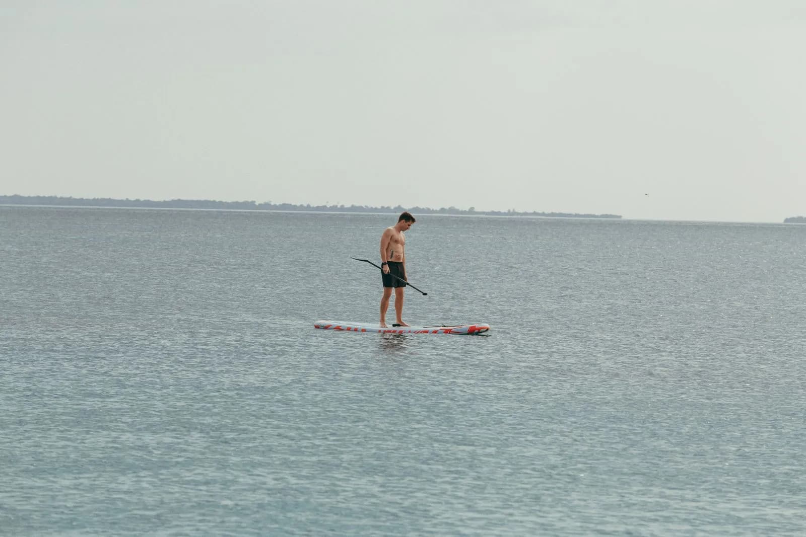 Young man standing on a paddle board in the middle of a calm ocean during a summer vacation trip