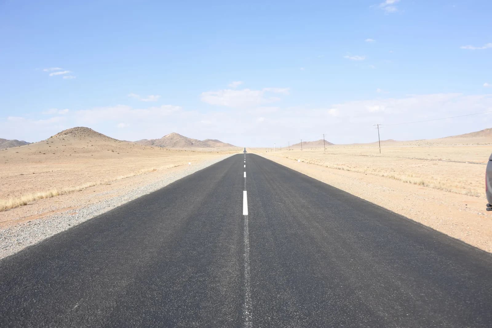 Empty asphalt road stretching through a vast arid desert landscape under a clear blue sky