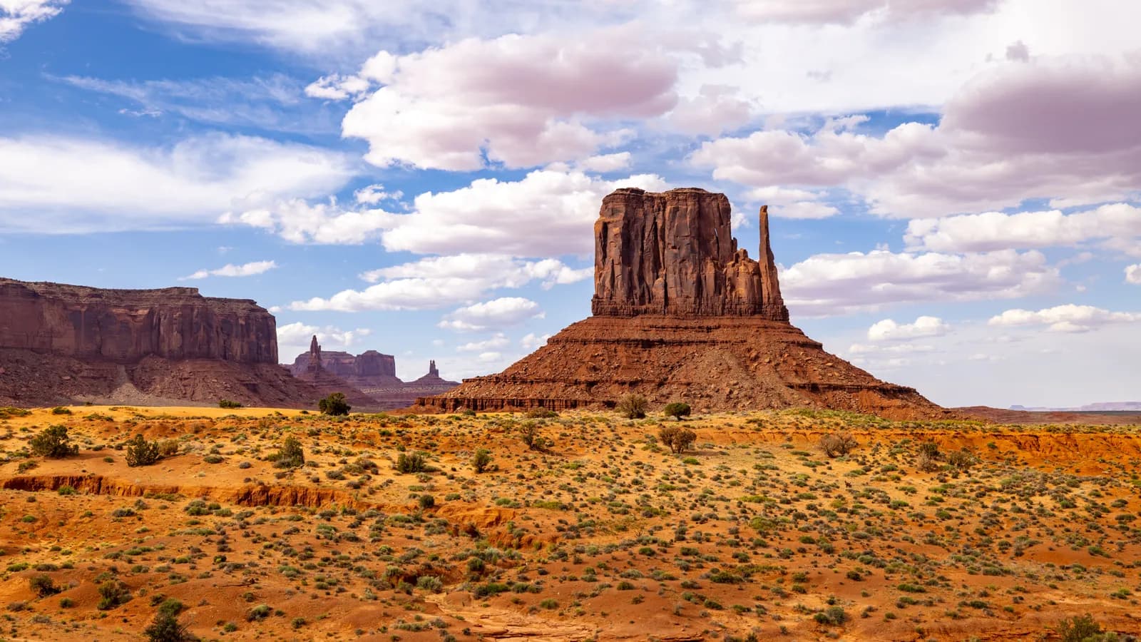 Scenic view of monument valley butte rock formations under a bright blue sky with white clouds