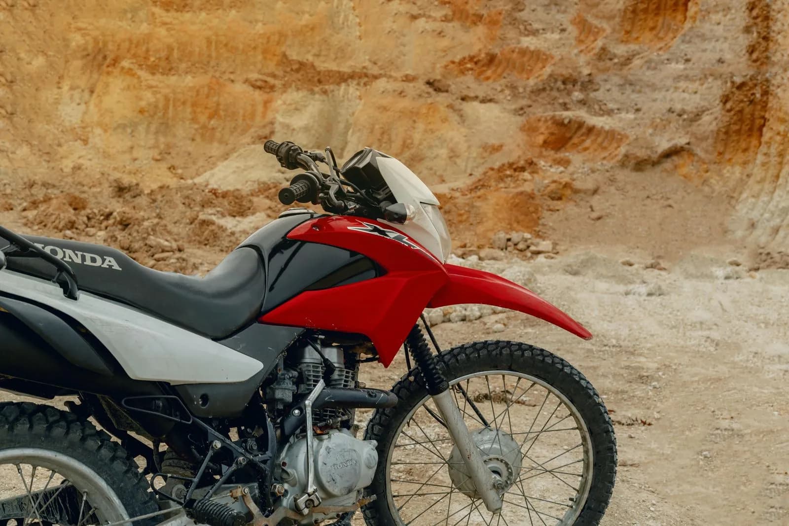 Red and white dirt bike parked in a sandy quarry for off road adventure and extreme sports travel